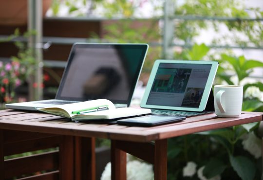 Deux portables ouverts sur une table accompagnées d'un carnet d'écriture.