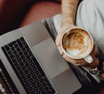 Personne qui tient une tasse de café dans ses mains en regardant son ordinateur.