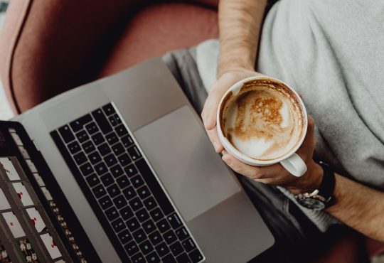 Personne qui tient une tasse de café dans ses mains en regardant son ordinateur.